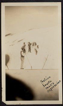 An undated black and white image showing men shoveling snow with shovels on the highway. Writing on the picture reads "Notice Fourth Man's Expression." One of the men in the picture is wearing sunglasses and smiling. Another has his thumb to his nose.