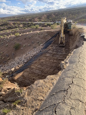 An excavator rebuilds the slope of State Route 190 over Argus Grade using benched construction.