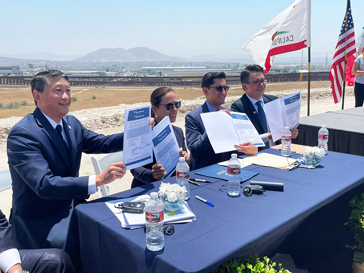Photo of CalSTA secretary David Kim sitting on a panel with three other people and holding up a signed document