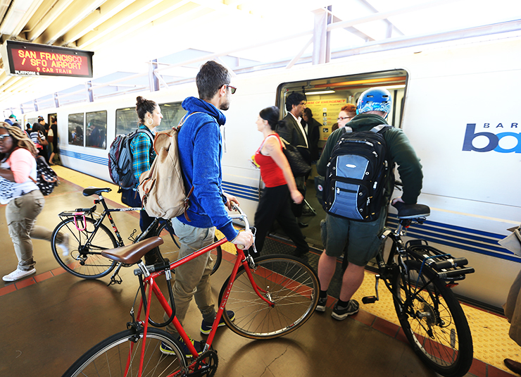 Photo taken inside a BART station in the bay area, showing passengers getting on and off the train, three people with bicycles in tow.